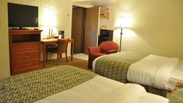 A hotel room with two beds, a desk, a television, and a lamp.