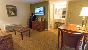 Habitación de hotel con televisión, escritorio, silla, cómoda, radiador y baño visible a través de una puerta abierta.