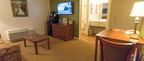 Une chambre d’hôtel équipée d’une télévision, d’un bureau, d’une chaise, d’une commode, d’un radiateur et d’une salle de bain visible à travers une porte ouverte.