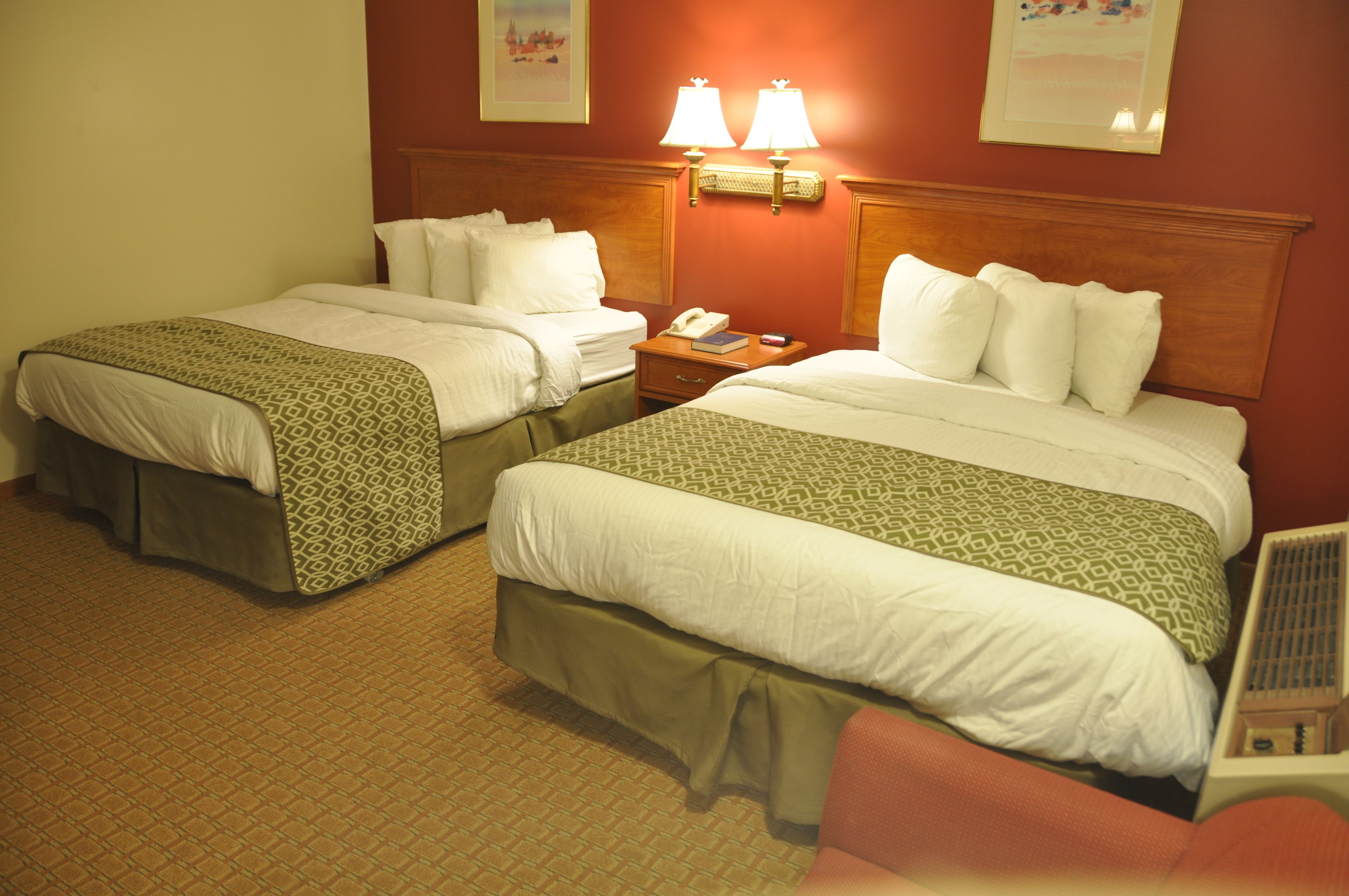 A hotel room with two single beds, a nightstand with a lamp, and a small table.