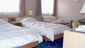 Una habitación de hotel con dos camas, un escritorio, una silla y una ventana con cortinas.