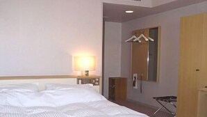Una habitación de hotel con cama, mesita de noche con lámpara, armario y espejo.