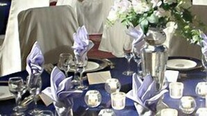 Mesa de comedor formal dispuesta con varios puestos individuales, incluyendo platos, vasos y cubiertos.