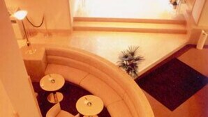 Un área de estar con asientos curvos, varias mesas redondas y sillas, una escalera que conduce a un nivel superior y vistas del espacio interior.