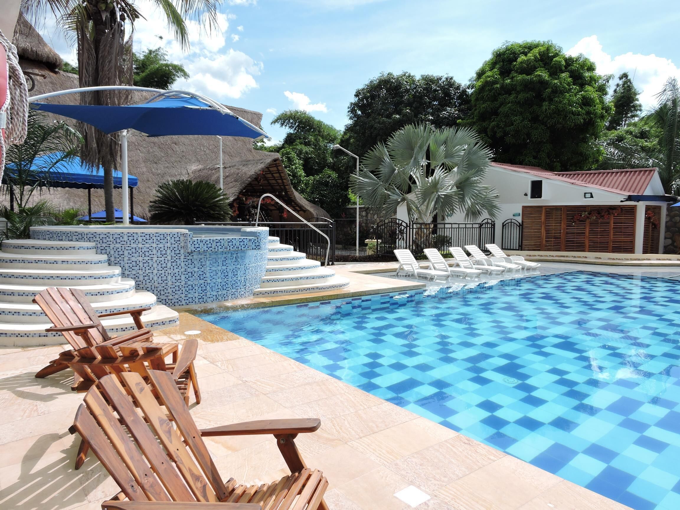 A swimming pool with checkered tiles, wooden lounge chairs, and a blue umbrella.