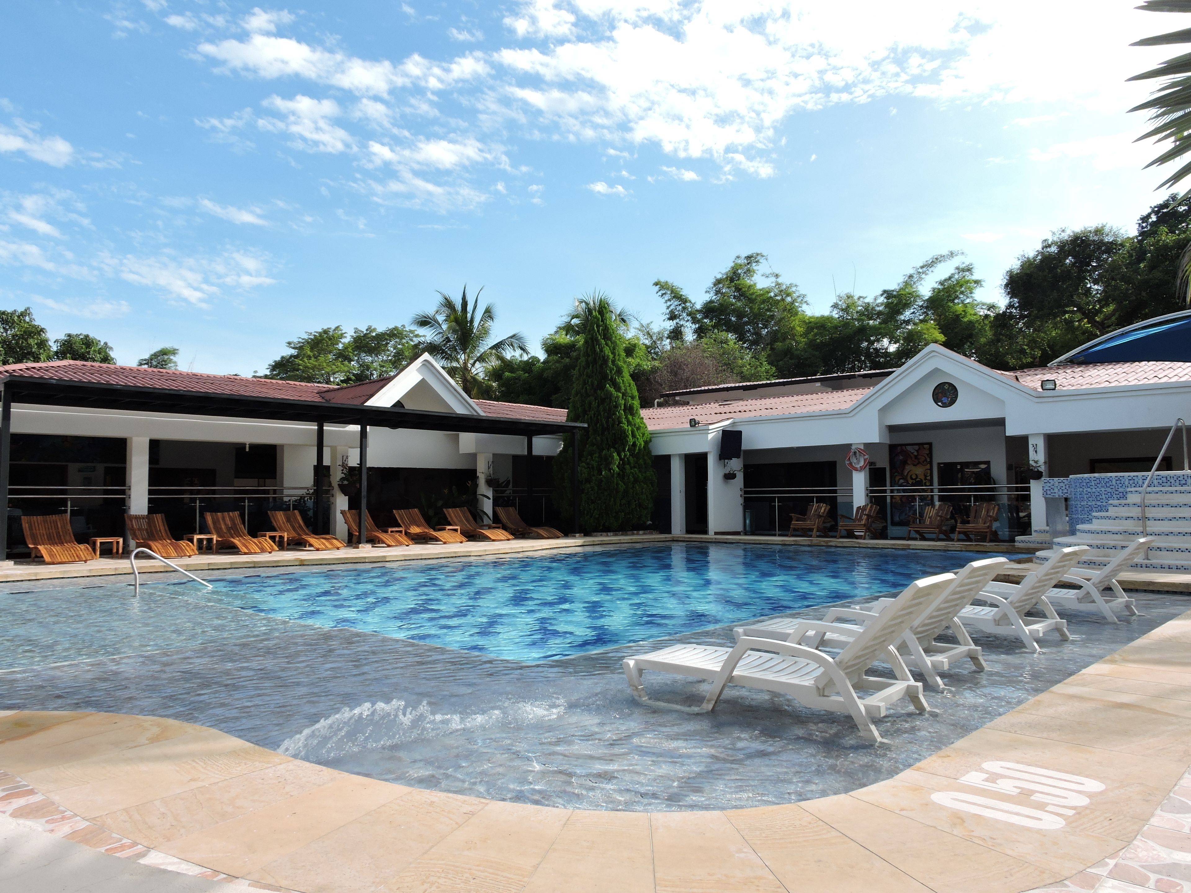 A pool area with lounge chairs, a covered seating area, and a building with a tiled roof.