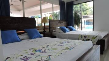 Habitación de hotel con dos camas, un ventanal con cortinas, ventilador de techo y vistas a una piscina y vegetación.