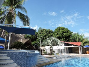 Un área de piscina con escalones de cerámica, sillas de descanso y sombrillas.