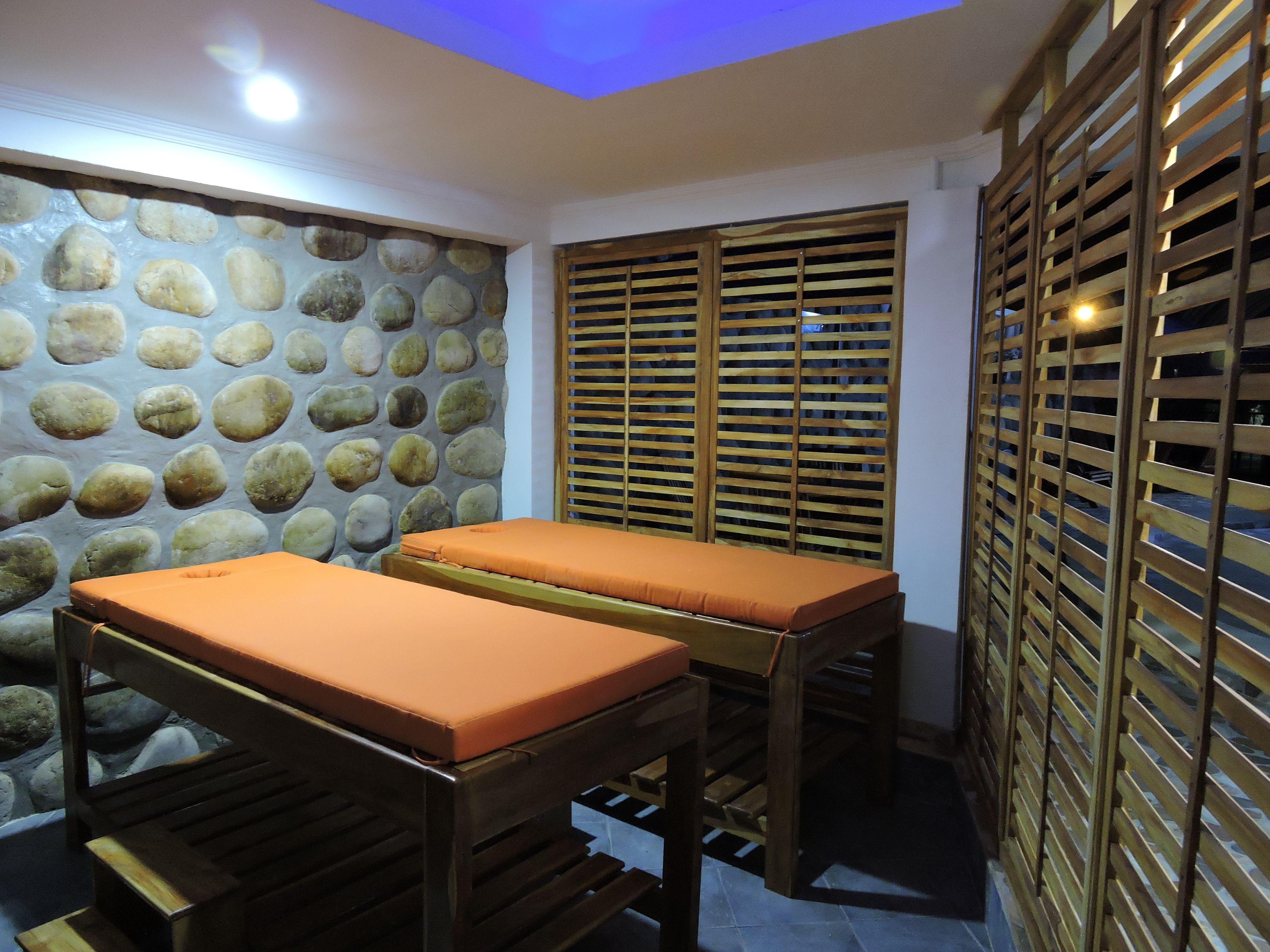 A spa room with two wooden massage tables, a stone wall, and wooden privacy screens.