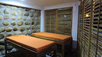 A spa room with two wooden massage tables, a stone wall, and wooden privacy screens.