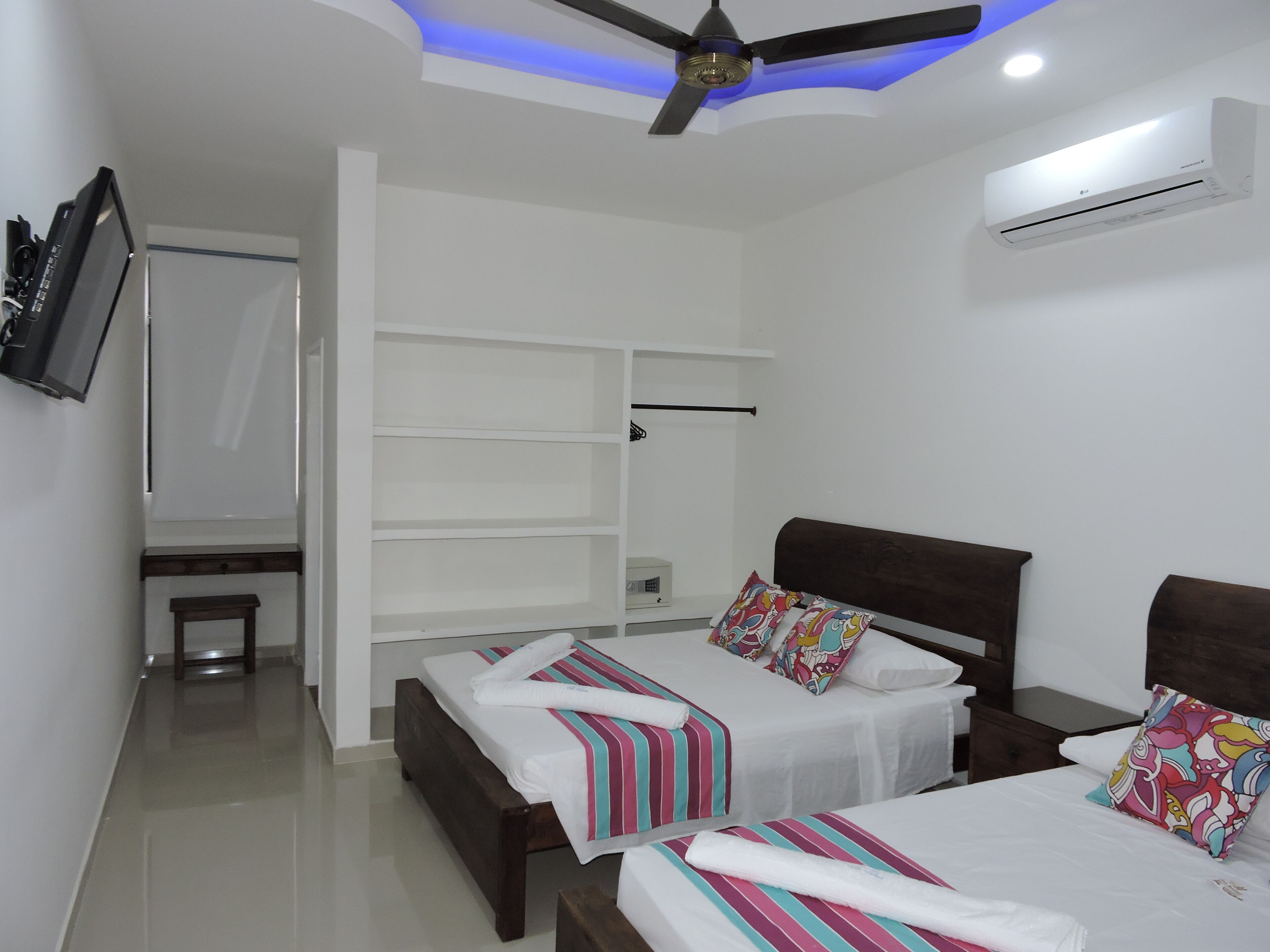 Un dormitorio moderno con dos camas, un ventilador de techo, un equipo de aire acondicionado y un televisor montado en la pared.