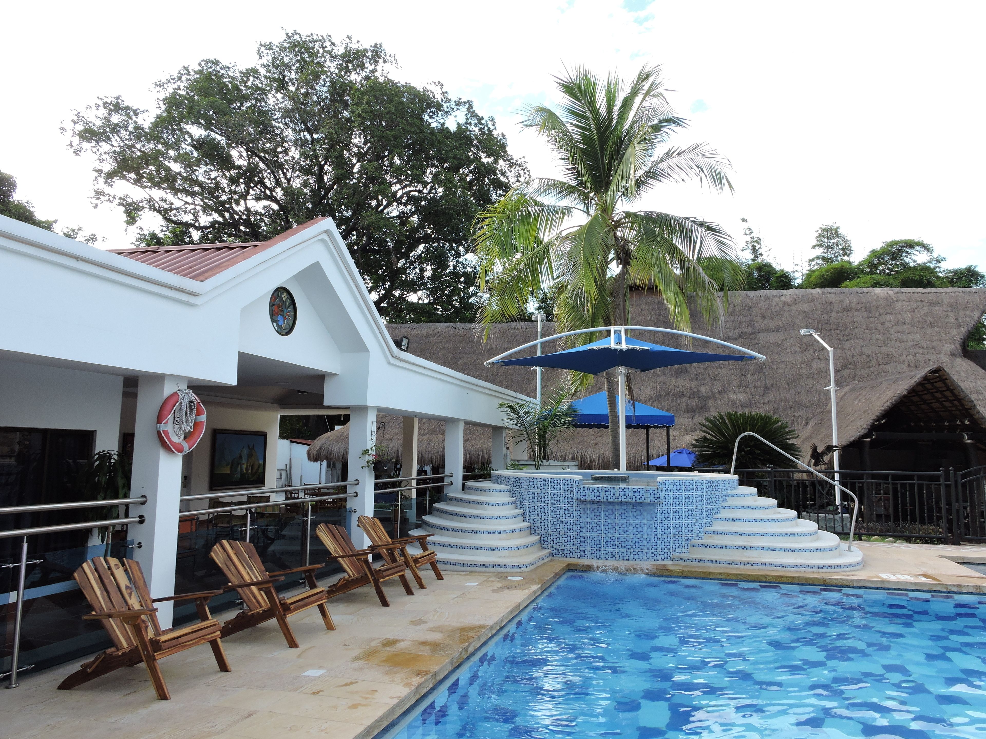 Un área de piscina con sillas de descanso, un flotador salvavidas y una estructura de techo de paja.