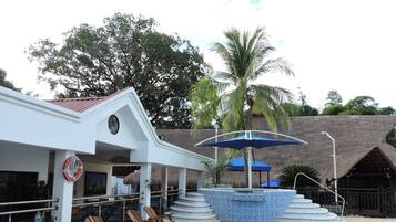 A pool area with lounge chairs, a lifebuoy, and a thatched-roof structure.