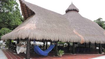 A thatched-roof structure with a hammock and potted plants.