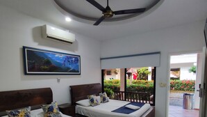 Habitación de hotel con dos camas, ventilador de techo, aire acondicionado, un cuadro y vista al jardín exterior.