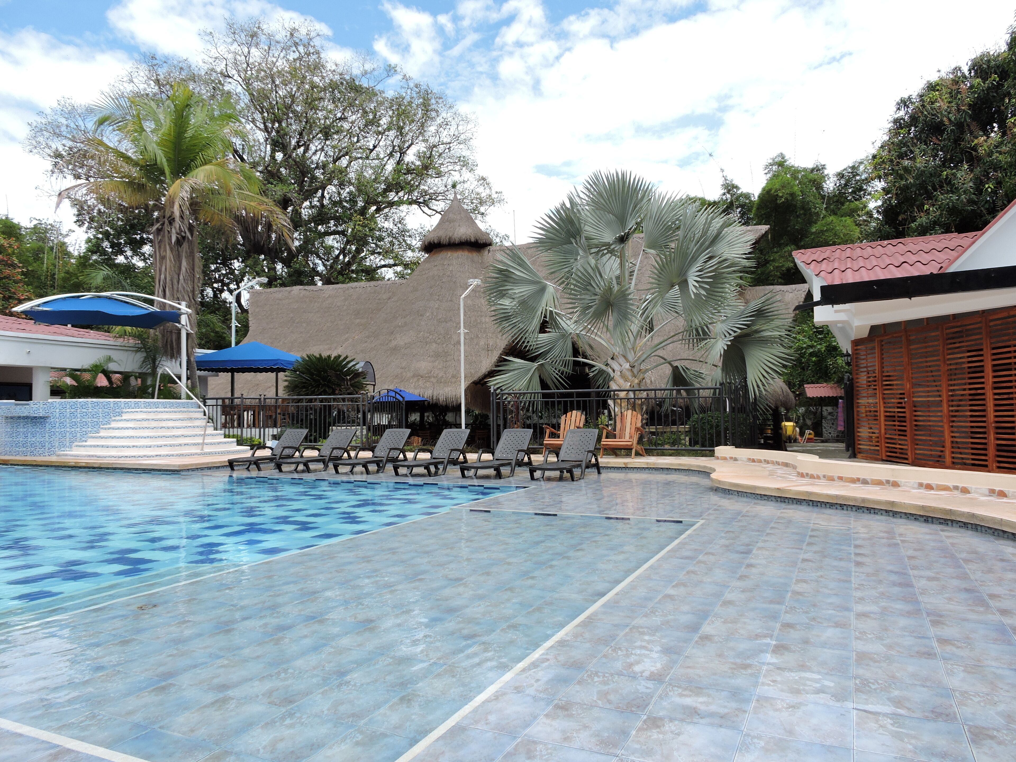 Ein Swimmingpool mit Liegestühlen, ein Gebäude mit Reetdach und Palmen.