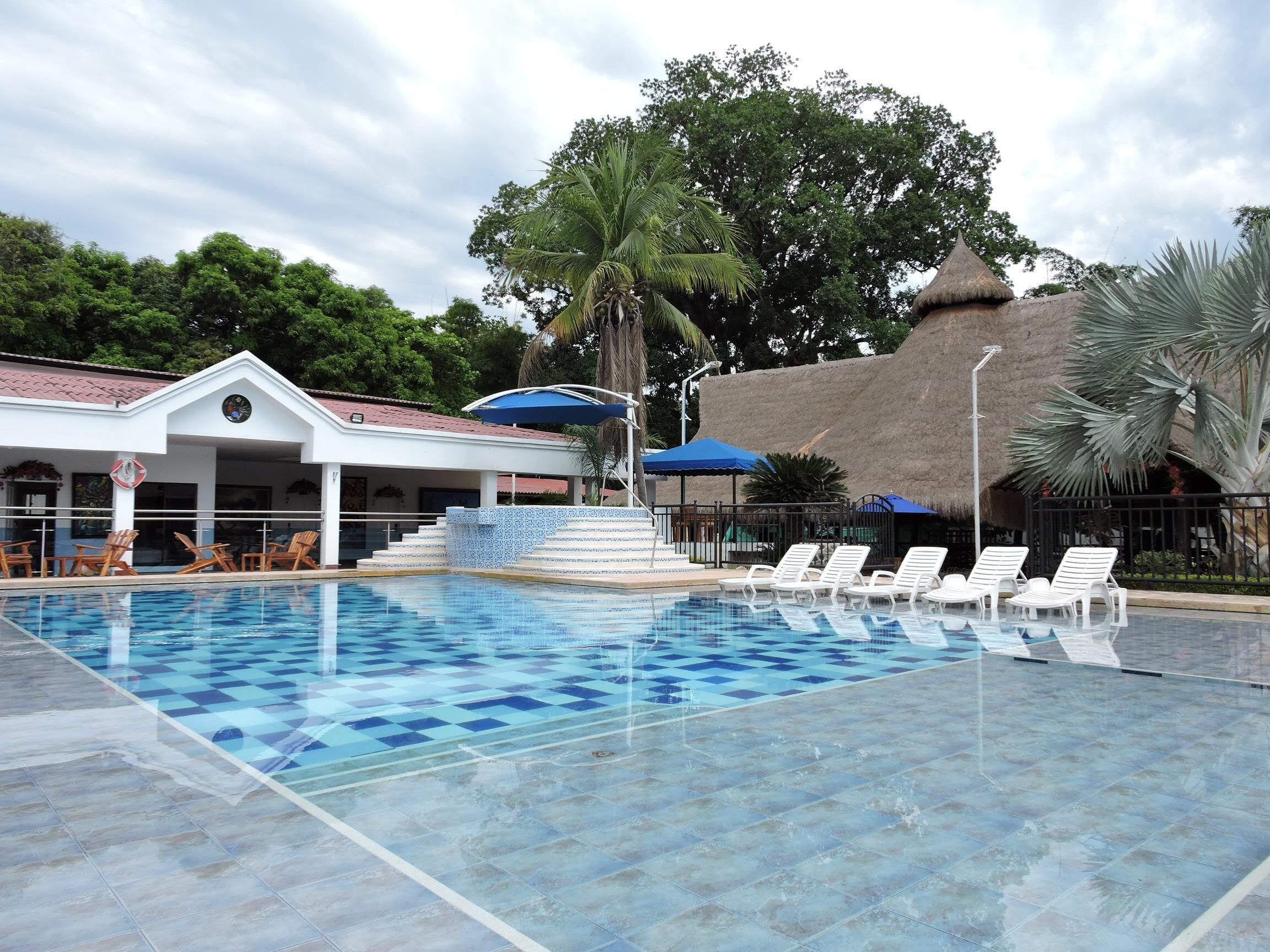A swimming pool with checkered tiles, lounge chairs, and a building with a thatched roof.