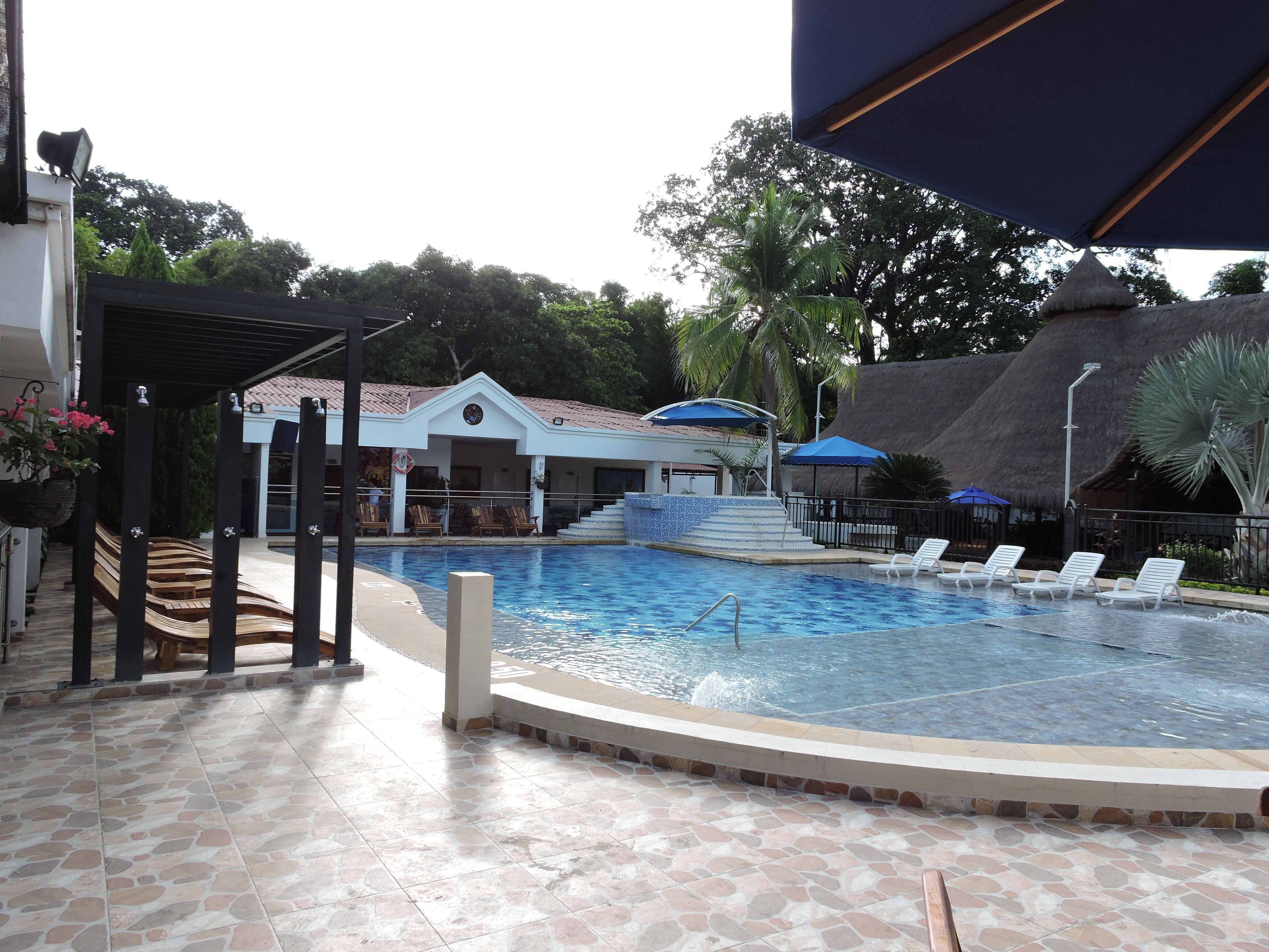 A swimming pool with lounge chairs, a covered seating area, and a building with a tiled roof.
