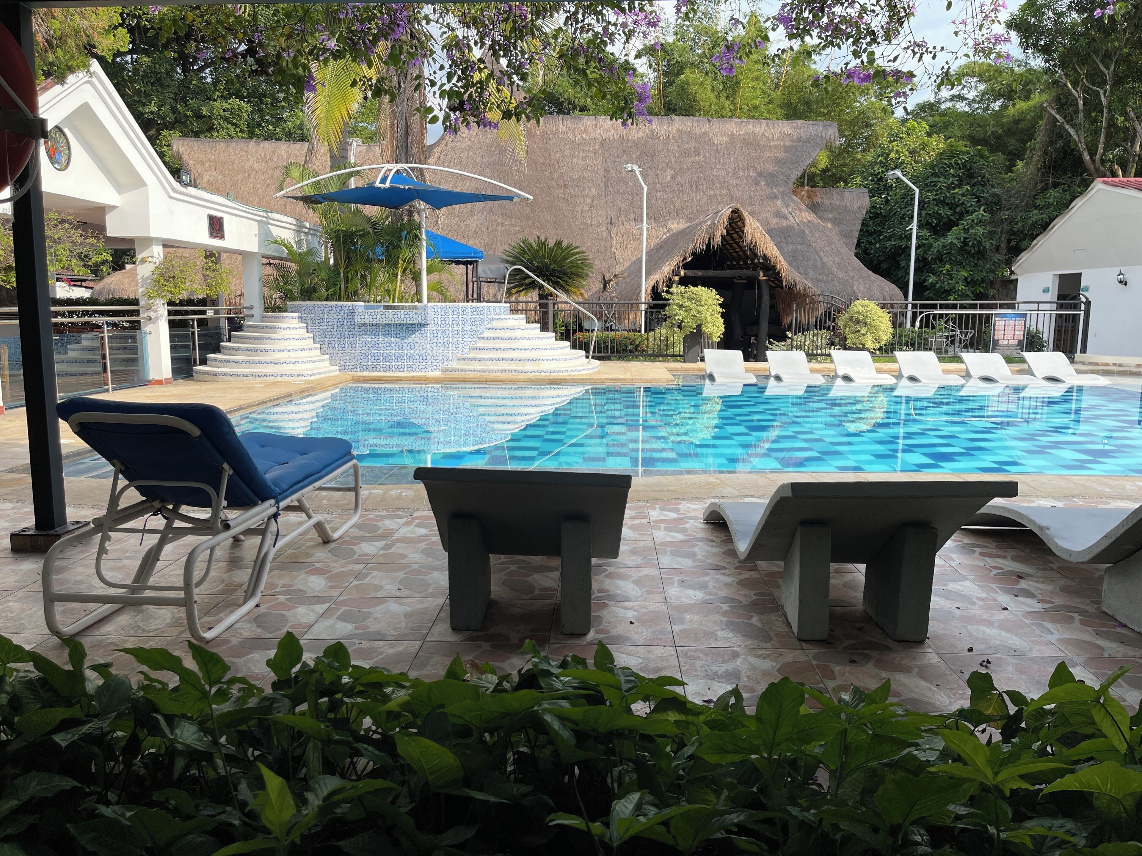 Une piscine avec des chaises longues, un parasol bleu et une structure à toit de chaume.