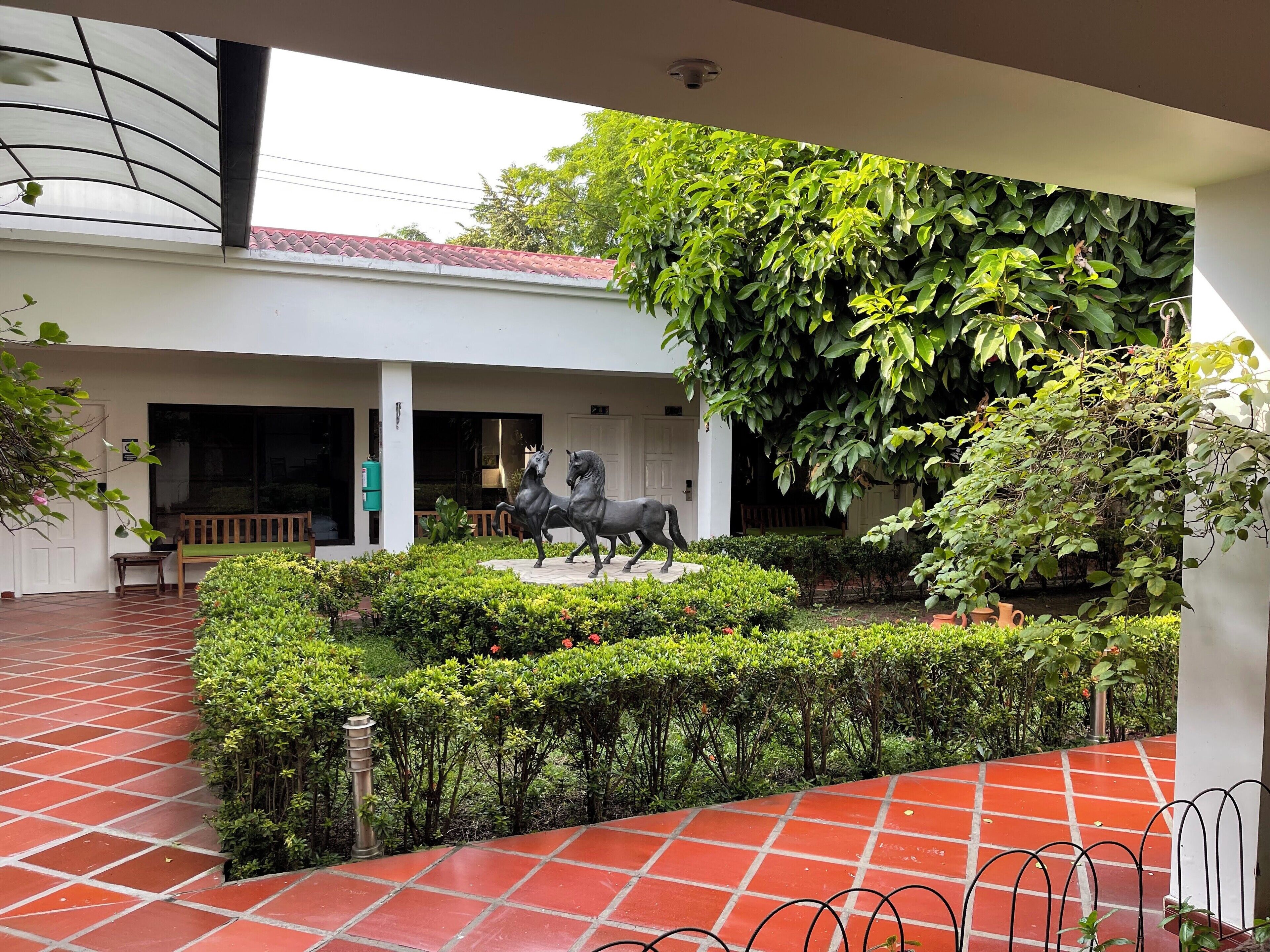 A courtyard with a statue of two horses, a bench, and a tiled floor.