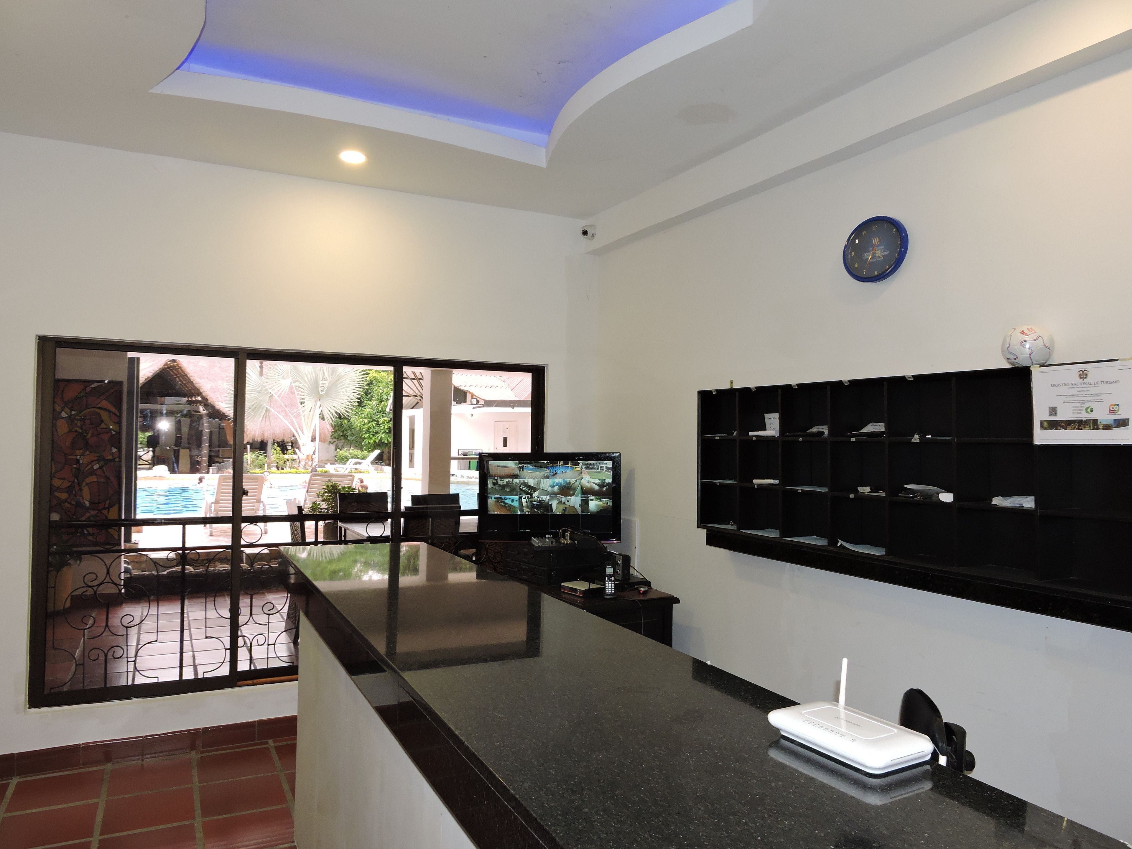 A reception area with a glass partition, a flat-screen TV, a whiteboard, and a sign on the wall.