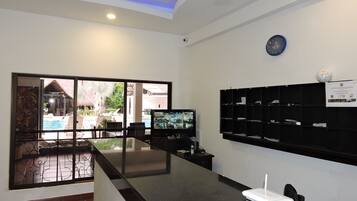 A reception area with a glass partition, a flat-screen TV, a whiteboard, and a sign on the wall.