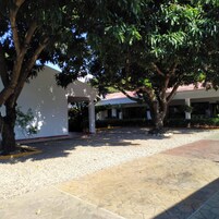 Un patio con un sendero de grava, una zona de estar techada y un edificio con tejado rojo.