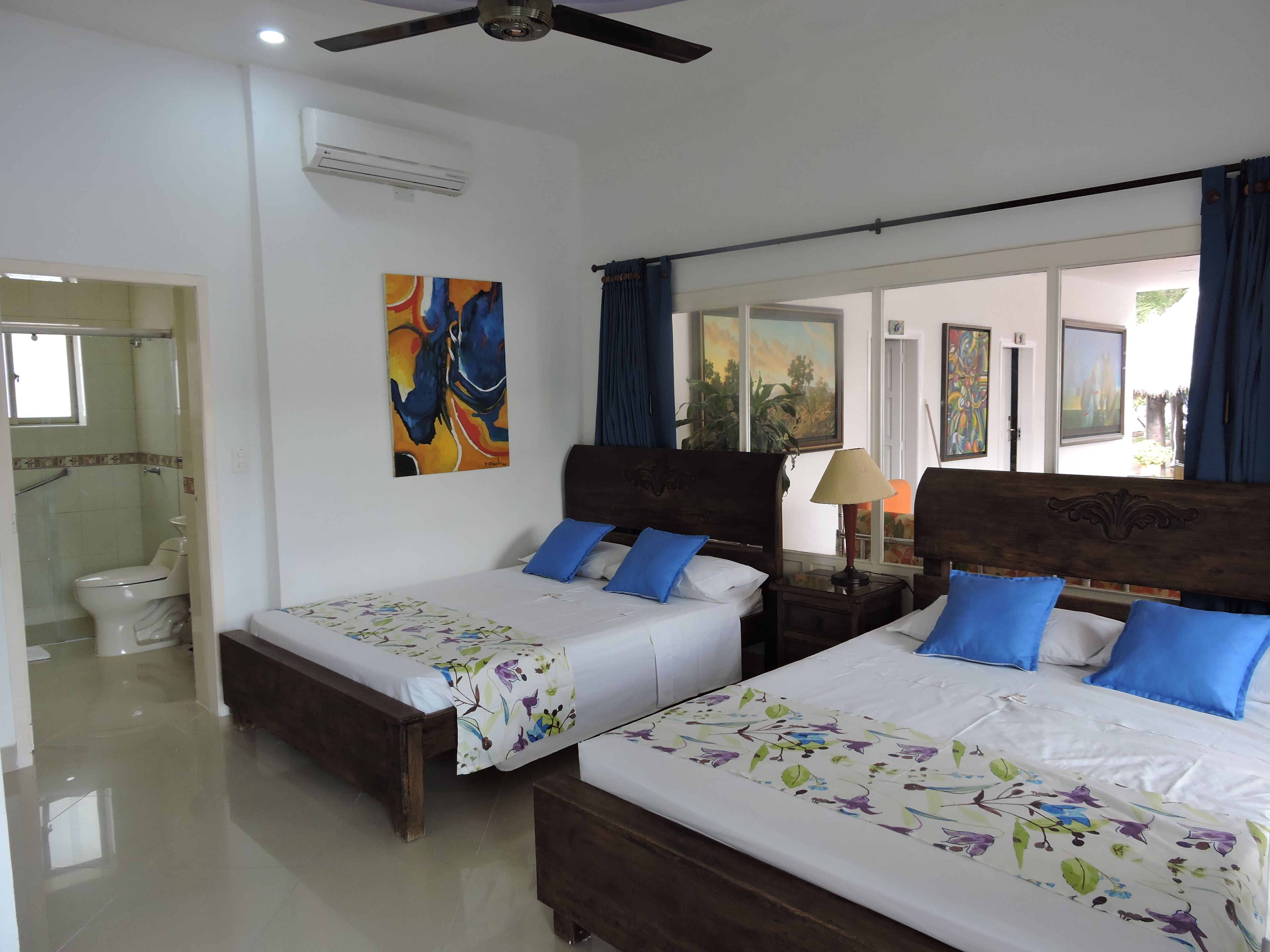 A hotel room with two wooden beds, a bathroom, and a view of the outdoors.