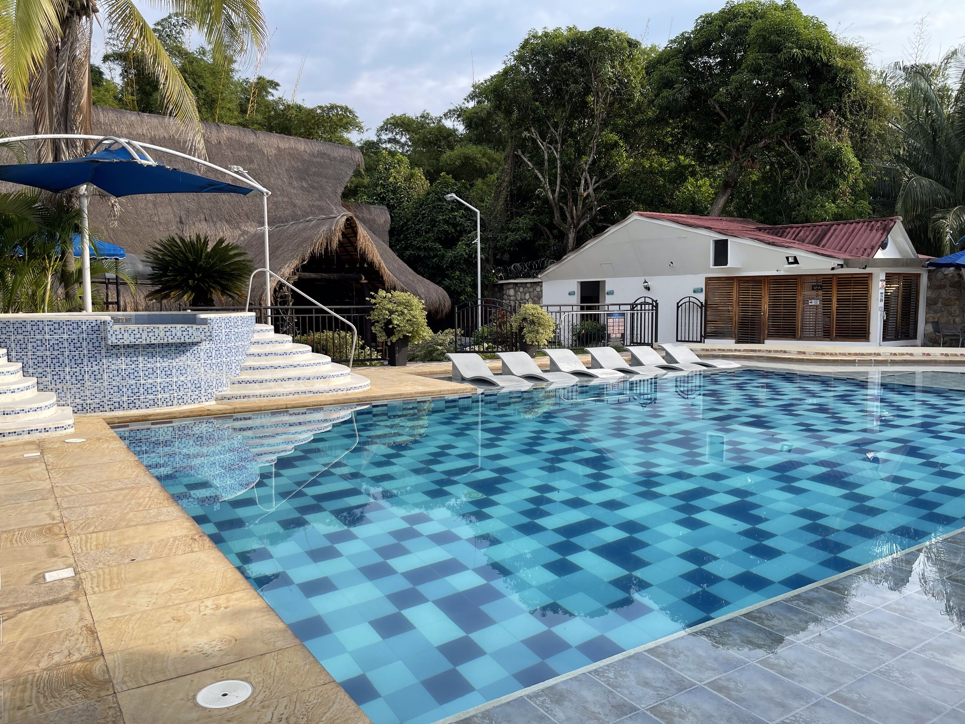 Una piscina con diseño a cuadros, sillas de descanso y una estructura de techo de paja.