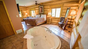 A log cabin bedroom with a large bed, a sitting area with a chair, and a bathroom with a bathtub. - Alpine Meadows Resort (Clearwater)