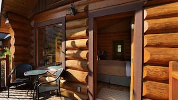 Eine Blockhütte mit einer Terrasse, komplett mit Tisch, Stühlen, einem Bett und einem Fenster mit Jalousien.