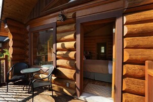 Una cabaña de troncos con un patio amueblado, que incluye una mesa, sillas, una cama y una ventana con persianas.