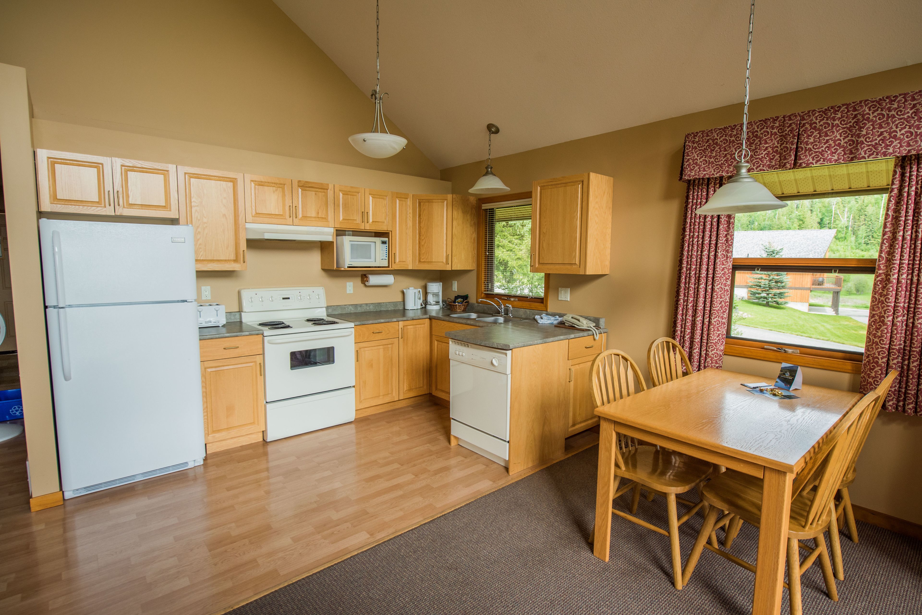A kitchen with wooden cabinets, a refrigerator, microwave, stove, and a dining table with chairs.