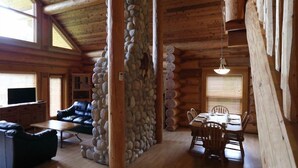 A log cabin interior with a stone pillar, a sofa, a dining table set, and a television. - Alpine Meadows Resort (Clearwater)