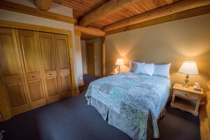 A bedroom with a large bed, wooden wardrobe, two bedside tables with lamps, and a carpeted floor.