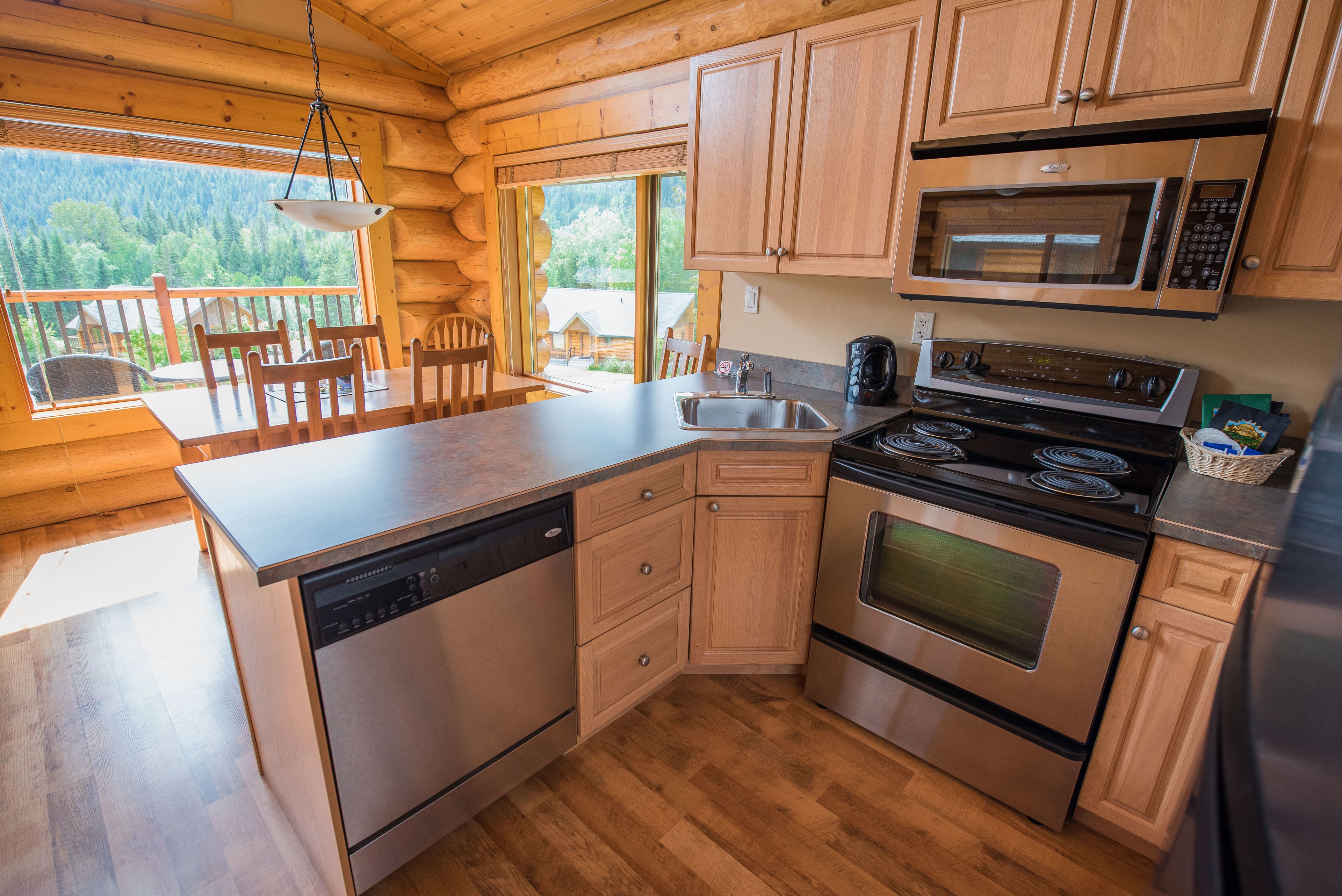 A modern kitchen with wooden cabinets, stainless steel appliances, and a large window overlooking a forested area.