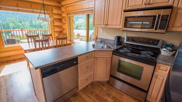 A modern kitchen with wooden cabinets, stainless steel appliances, and a large window overlooking a forested area.