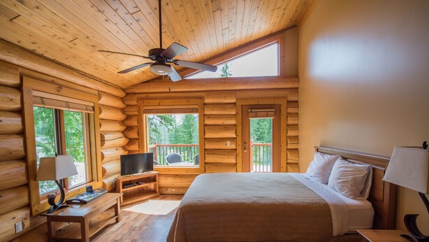 A log cabin bedroom with a bed, a television, a desk, and a window overlooking the outdoors. - Alpine Meadows Resort (Clearwater)