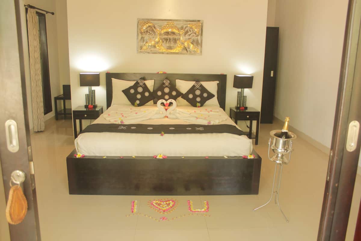A neatly arranged bedroom with a large bed, two bedside tables with lamps, a decorative wall piece, and a bottle of champagne on a stand.