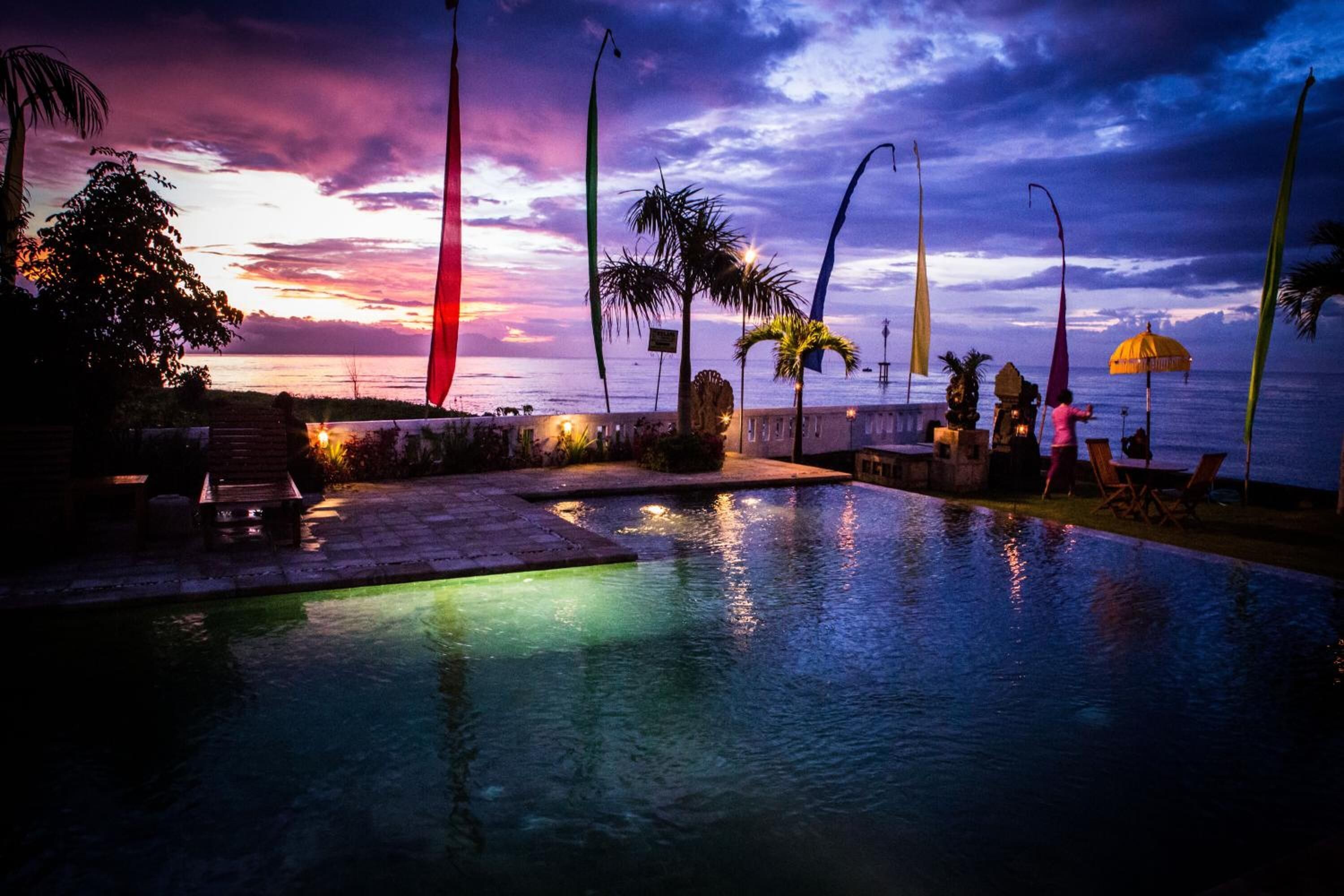 A pool area with a sunset view, palm trees, and lounge chairs.