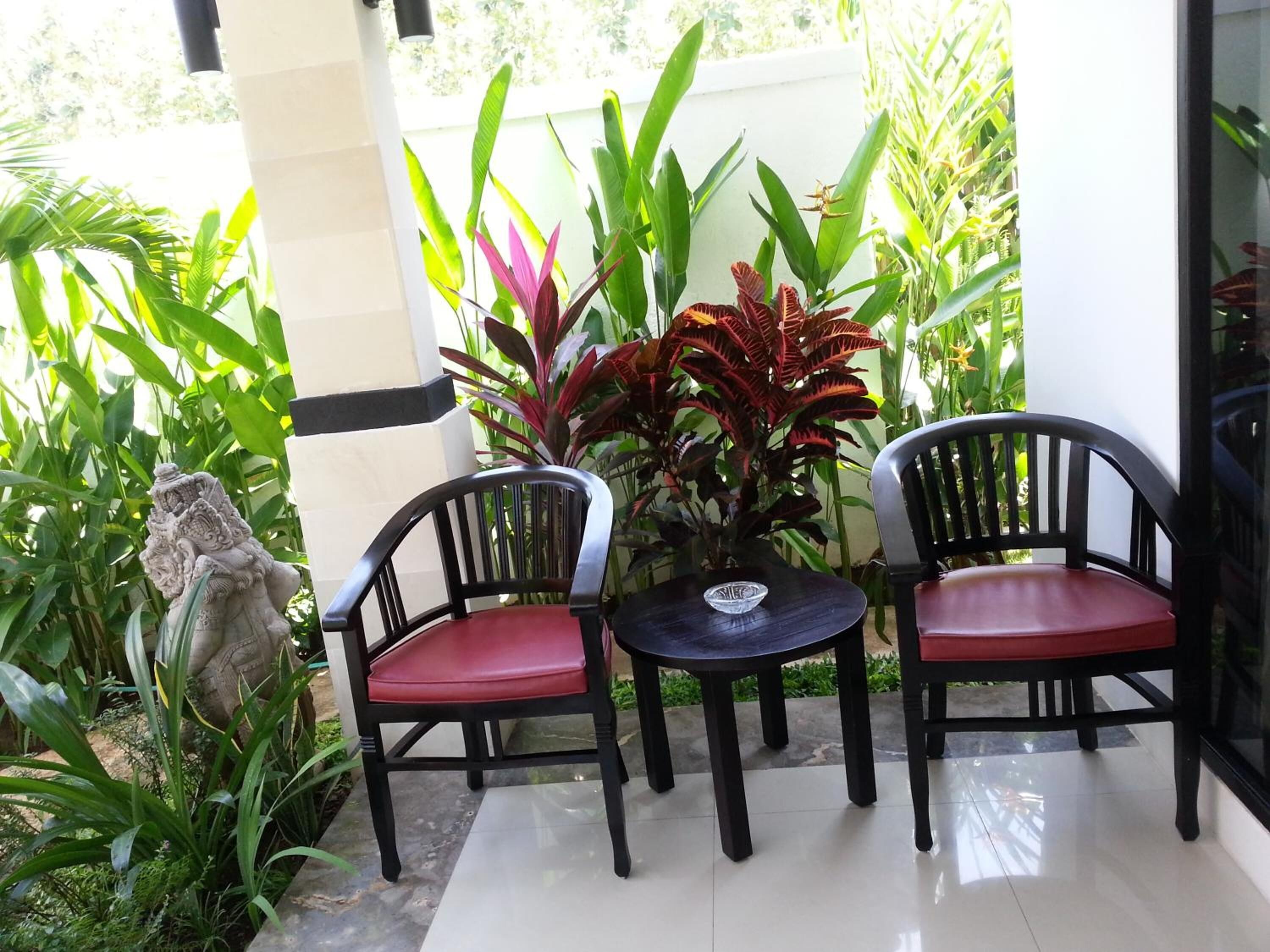 Un patio con dos sillas negras con cojines rojos, una mesita redonda y varias plantas.