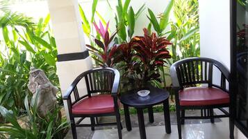 Un patio con dos sillas negras con cojines rojos, una mesita redonda y varias plantas.