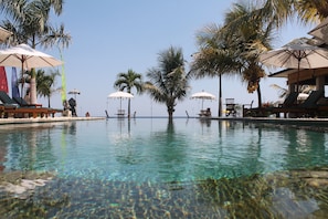 Une piscine aux eaux cristallines, agrémentée de parasols et de chaises longues, le tout entouré de palmiers.