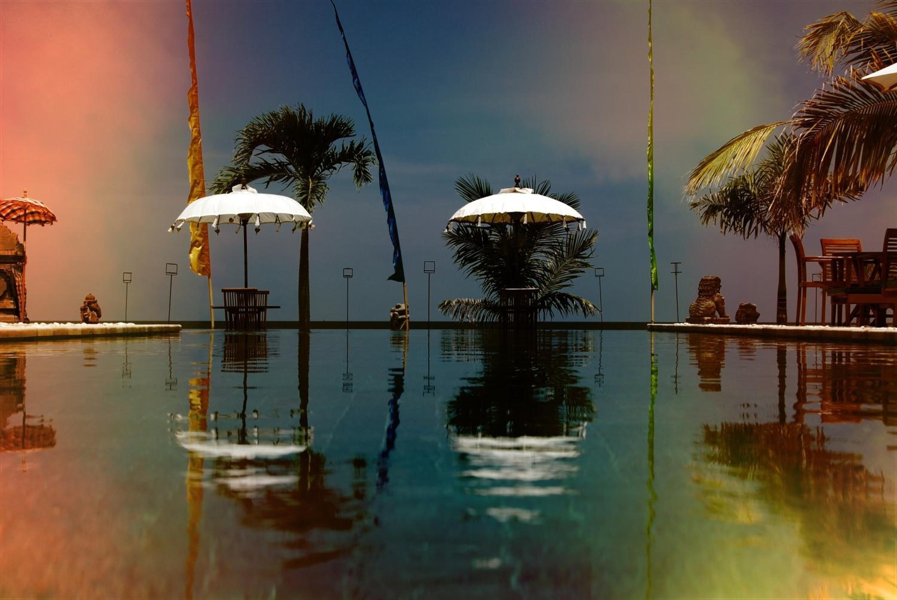 Una piscina con sombrillas, palmeras y cielo despejado.