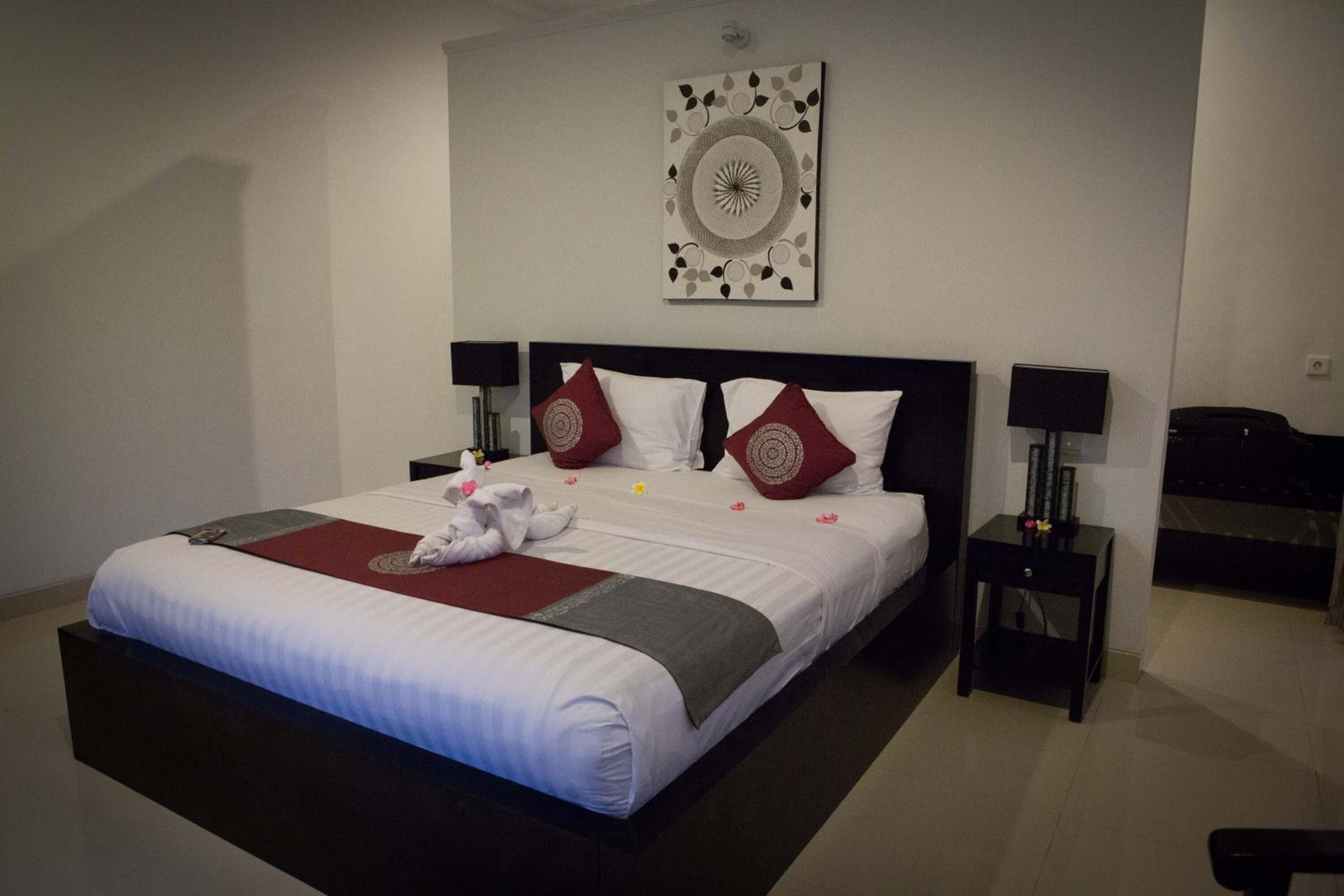 A neatly made bed with white linens, red and white pillows, and a decorative wall piece above it.