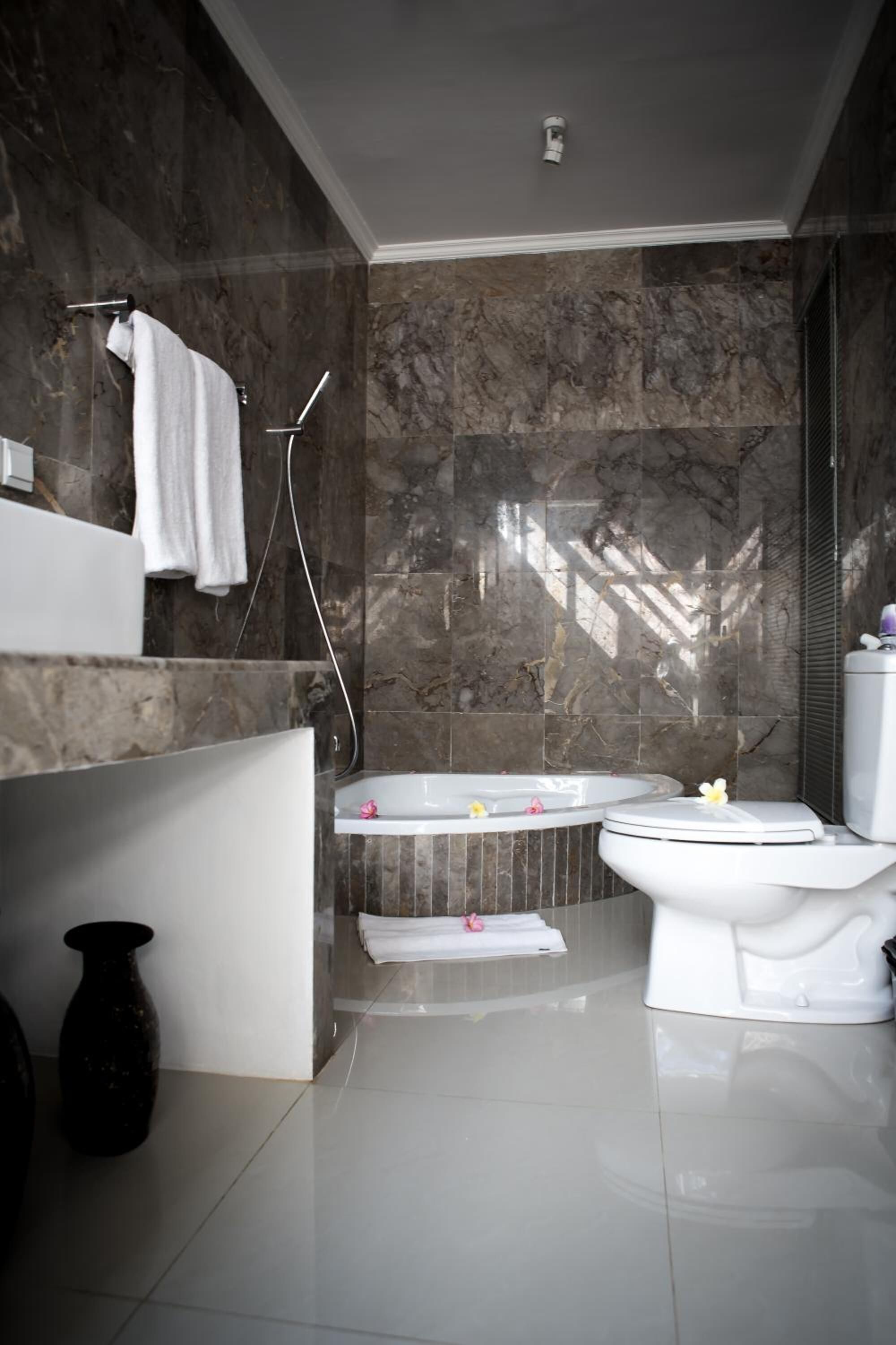 A modern bathroom with a marble wall, a bathtub, a toilet, and a shower.