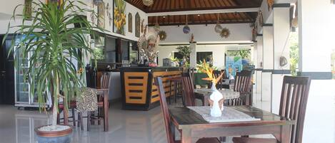 A spacious dining area with a wooden table and chairs, a potted plant, and a bar area in the background.