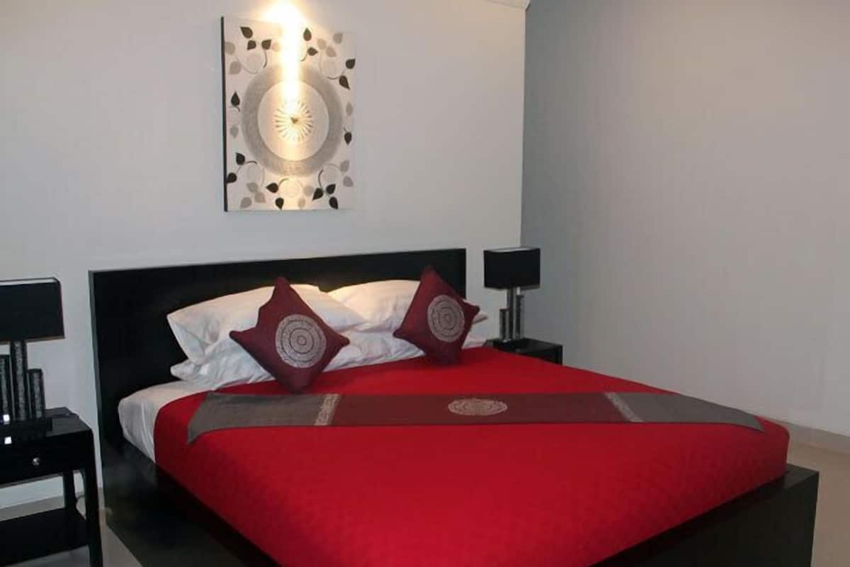 A modern bedroom with a large bed, red bedding, two bedside tables with lamps, and a wall-mounted light fixture.
