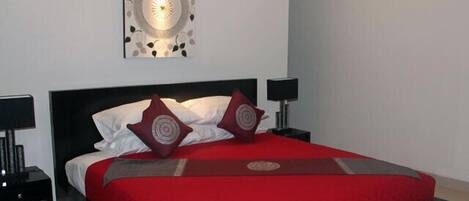 A modern bedroom with a large bed, red bedding, two bedside tables with lamps, and a wall-mounted light fixture.