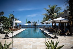 Un área de piscina con sillones y sombrillas, rodeada de palmeras y vista al mar.